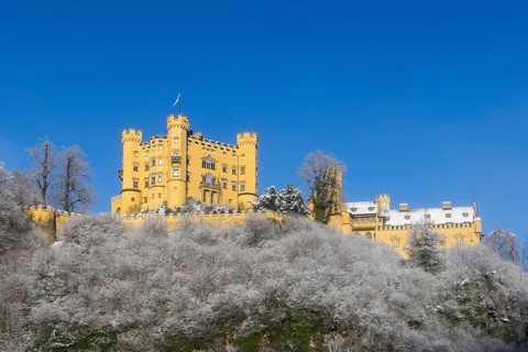 A castle majestically enthroned on a snow-covered hill with a blue sky, Hohenschwangau Castle,