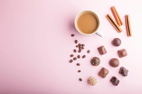 Different chocolate candies and a cup of coffee on a pink pastel background. top view, flat lay,