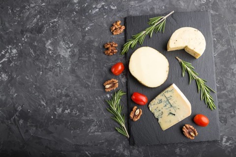 Blue cheese and various types of cheese with rosemary and tomatoes on black slate board on a black