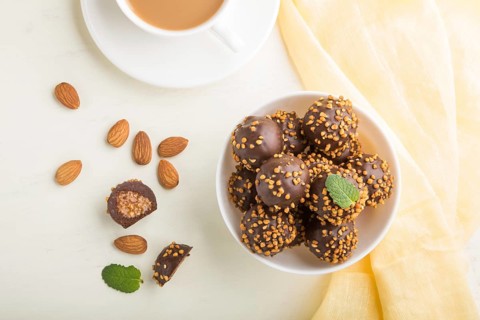 Chocolate caramel ball candies with almonds and a cup of coffee on a white wooden background and
