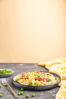 Quinoa porridge with green pea, corn and dried tomatoes on ceramic plate on a gray and orange