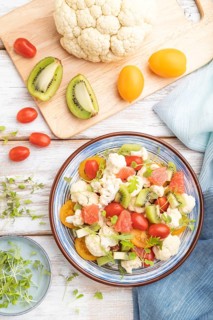 Vegetarian salad of cauliflower cabbage, kiwi, tomatoes, microgreen sprouts on white wooden