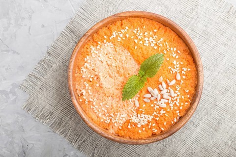 Carrot cream soup with sesame seeds in wooden bowl on a gray concrete background with linen textile