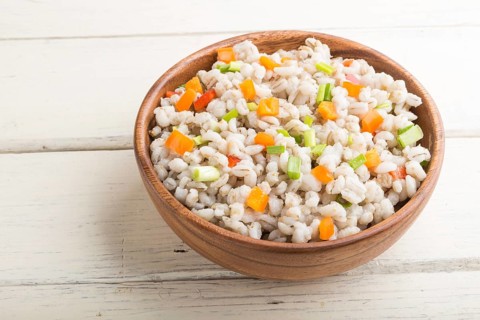 Pearl barley porridge with vegetables in wooden bowl on a white wooden background. Side view, close