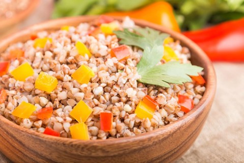 Buckwheat porridge with vegetables in wooden bowl on a white wooden background and linen textile.