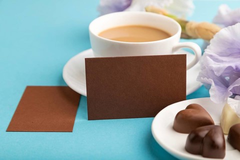 Brown business card with cup of cioffee, chocolate candies and iris flowers on blue pastel