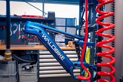 Blue bicycle frame in a workshop with tools in the background, Waldbike Manufaktur, bicycle