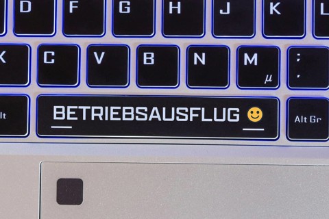 Company outing symbol image: Keyboard labelled BETRIEBSAUSFLUG, with a cheerful emoji next to it
