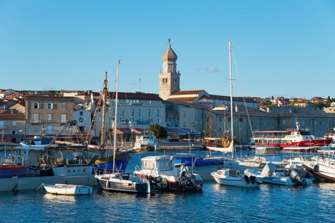 Coastal town at sunset with harbour and boats, in the background a church and historical buildings,