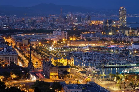 Aerial view of Barcelona city skyline with city traffic and port with yachts illuminated in the