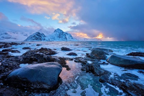 Beach of Norwegian sea on rocky coast in fjord on sunset in winter. Vareid beach, Lofoten islands,