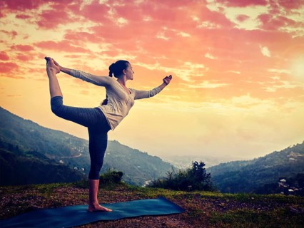 Woman doing yoga asana Natarajasana, Lord of the dance pose outdoors at waterfall in Himalayas.