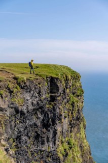 Tourist at the edge of a rock cliff, steep coast, at Reynisfjara beach, Vik, South Iceland,