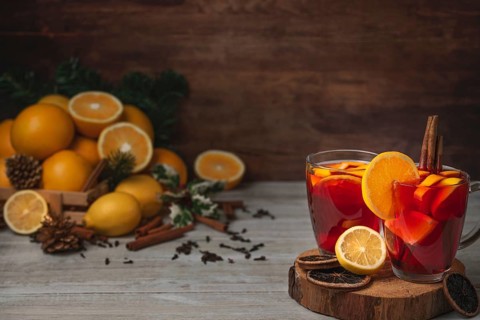 Wooden basket with oranges and lemons, two glass cups with punch, cloves and cinnamon sticks,