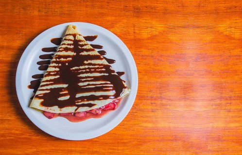 Crepe with chocolate cream and strawberry on wooden table. Sweet strawberry crepe with chocolate
