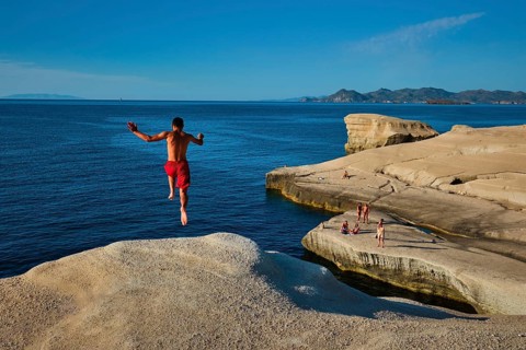 Sarakiniko, Greece, May 23, 2019: Young tourists jump off the white rocks cliff on famous tourist