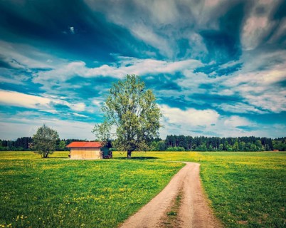 Vintage retro effect filtered hipster style image of rural road in summer meadow with wooden shed.