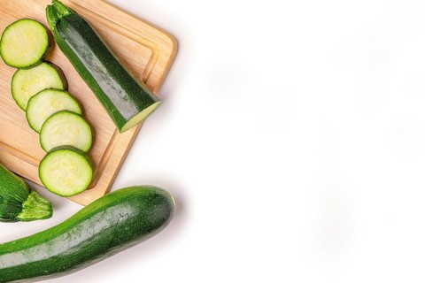 Courgettes (Cucurbita pepo), whole and cut open, on wooden board, on white, copy room