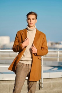 Spring, autumn outfit. Street fashion. Young man in checkered trousers, sweater wraps wool coat
