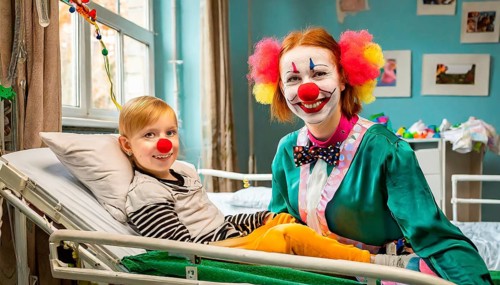 A female clown, a clinic clown, in mask, red nose and costume with a sick child in the clinic, AI