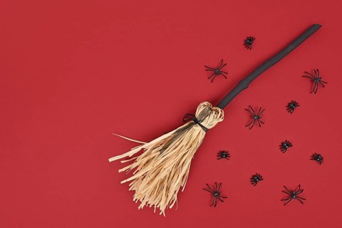 Halloween witch broom and spiders on dark red background with copy space