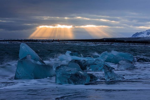 Waves breaking on icebergs on the black beach of Breidamerkursandur, sunset, near Jökullsarlon,