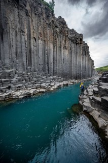 Tourist standing by the river in Stuðlagil Canyon, turquoise blue river between basalt columns,