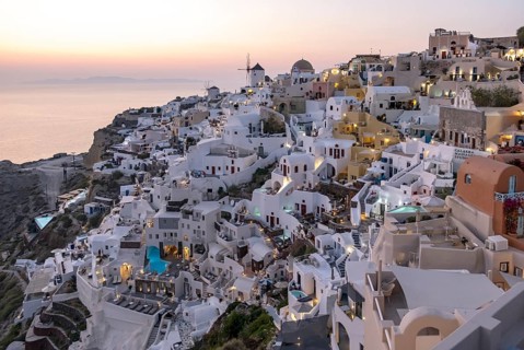Cliff-side houses, villas and windmill in the village of Ia seen from Oia Castle at dusk,