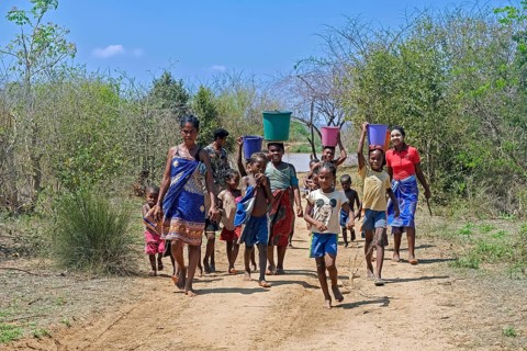 Malagasy women and children with buckets of water on their heads walking from river back to village