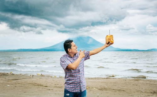 Young man vacationing and enjoying a coconut on the beach. Smiling man holding and pointing at a