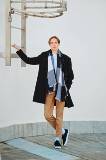 Full length portrait of young man in old wool coat, scarf and short trousers leaning to fire escape