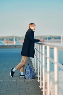 Young student with backpack in old wool coat, scarf and short trousers leaning to the railings