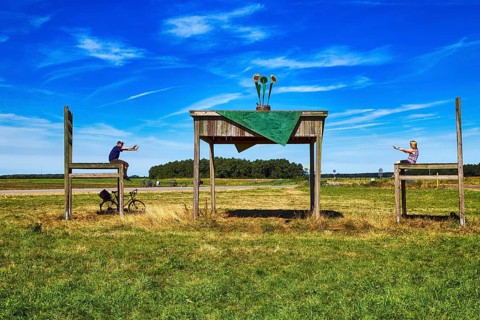 Oversized table with two chairs on a meadow, passers-by taking a break together, having fun, sunny