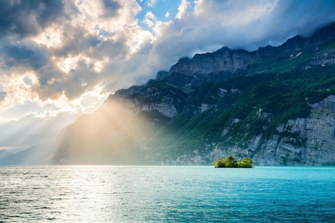 Evening sun rays on Lake Walen with chive island in the turquoise water and mountain range Schären