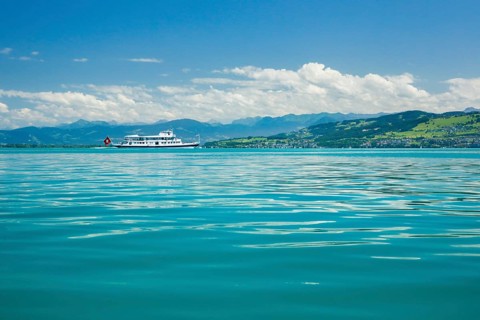 Course ship with Swiss flag on the turquoise waters of Lake Constance in front of the Austrian Alps