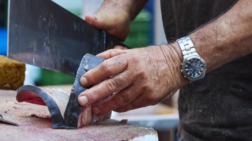 Man cuts tuna into strips with large knife, fish market, old town, Catania, east coast, Sicily,