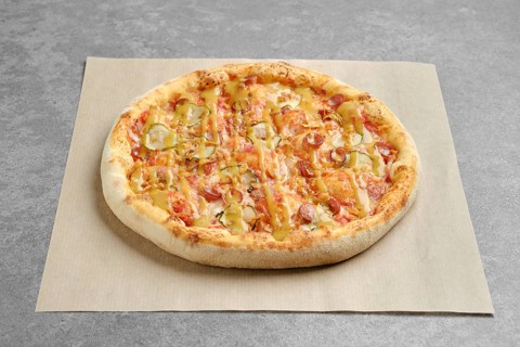 Top view of pizza with thin sausage and pickled cucumber on parchment paper