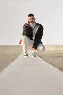 Urban fashion. Young man in loose clothes squats on the street
