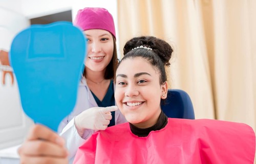 Satisfied patient in dental clinic looking at mirror, dentist next to satisfied patient smiling at