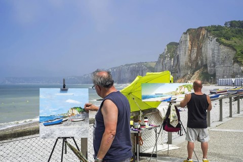 Landscape painters painting fishing boats, caïques on beach and sea cliffs at seaside resort Yport,