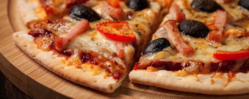 Letterbox panorama of sliced ham pizza with (capsicum) and olives on wooden board on table