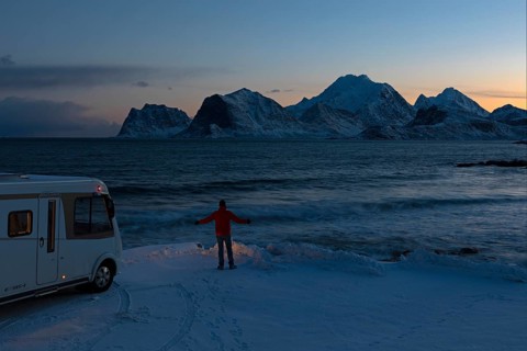 Motorhome in winter on pitch with view of fjord and snow-capped mountains, Storsandnes Beach,