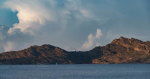Rocky coast with lighthouse Akrotiri Korakas with blue sea, dramatic cloudy sky Paros, Cyclades