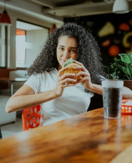 Beautiful latin girl enjoying a delicious hamburger in a restaurant. Portrait of afro girl holding