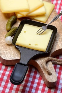 Raclette, cheese slices on wooden board and in raclette pans, Switzerland, Europe