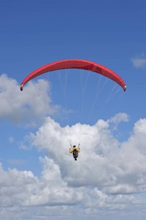 Paraglider in flight with red wing, canopy against blue cloudy sky, Brittany, France, Europe