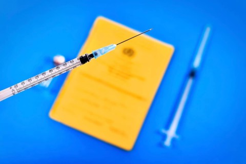 Vaccine concept with syringe in front of blurry vial and yellow international certificate of
