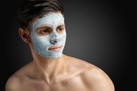 Portrait of a beautiful, relaxed young man with a face mask made of clay, skin care for face and