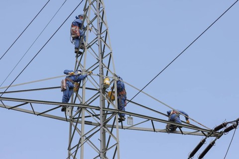 Industrial climber high up on an electricity pylon, workers wearing protective clothing, blue sky,