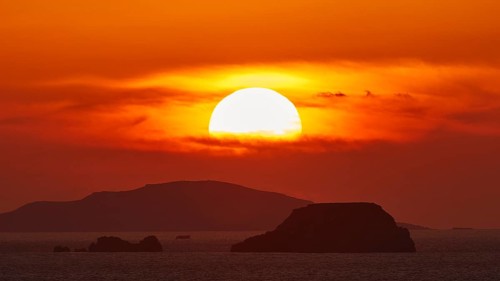 Sun setting over the sea with islands on the horizon, sky in intense orange tones, sunset, Kassos,